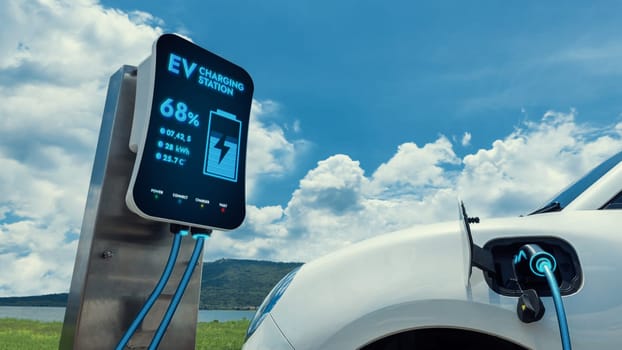 Electric car plugged in with charging station to recharge battery by EV charger cable with nature vacation background. Future innovative ev car and energy sustainability. Peruse