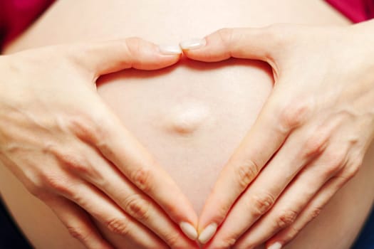 Woman hands made a heart on her stomach. Waiting for a child. The concept of pregnancy, motherhood, preparation and expectation.