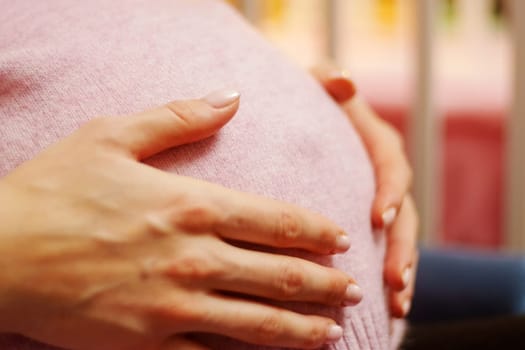 Woman is holding her stomach while sitting in a chair. A pregnant woman is expecting a baby