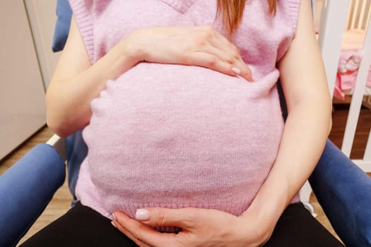 Woman is holding her stomach while sitting in a chair. A pregnant woman is expecting a baby