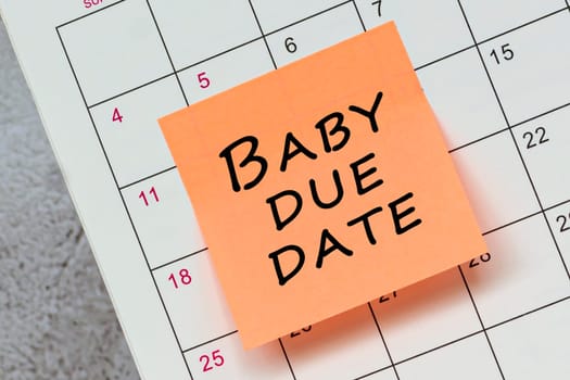 Baby due date written on a orange paper sticky note and stuck to a calendar background. Reminder concept.