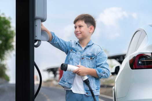 Little boy recharging eco-friendly electric car from EV charging station. EV car road trip travel concept for alternative transportation powered by clean renewable and sustainable energy. Perpetual