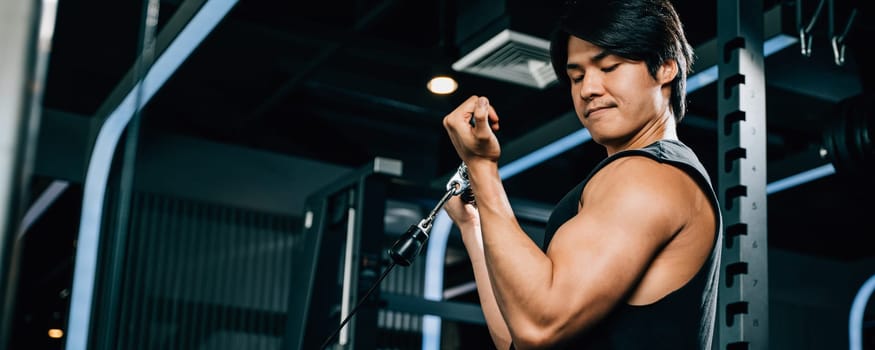 Concept of fitness and exercise - a muscular male athlete pulling a cable tricep rope during a strength training session. lifestyle and people concept