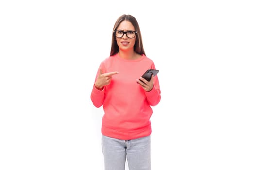 a young caucasian model woman with light makeup and dark straight hair dressed in a pink sweater uses a smartphone and talks about it.