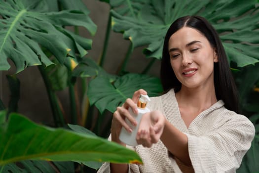 Tropical and exotic spa garden with bathtub in modern hotel or resort with woman in bathrobe holding beauty skincare product while enjoying leisure lush with greenery foliage background. Blithe