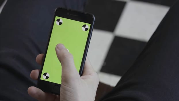 Man hands using mobile smartphone with green screen, over the shoulder view. Close up of man scrolling and tapping on Iphone screen with chroma key.
