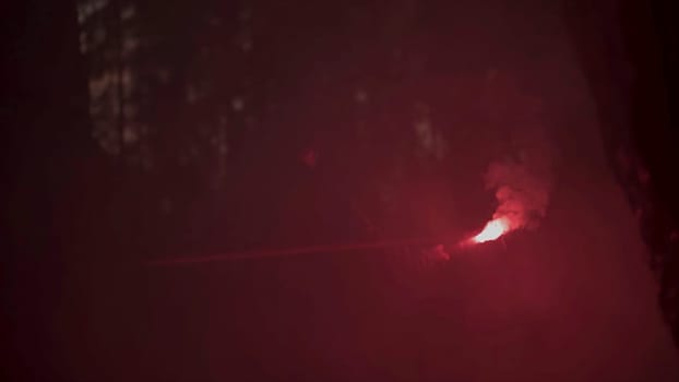 Young man found a narrow hole inside the cave and illuminates the way with red burning signal flare. Absolutely deep darkness around in grotto.