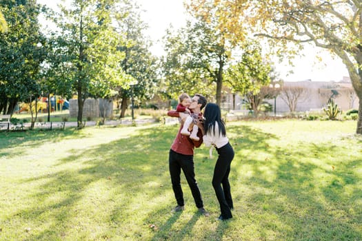 Mom hugs dad by the shoulders kissing a little girl in his arms. High quality photo