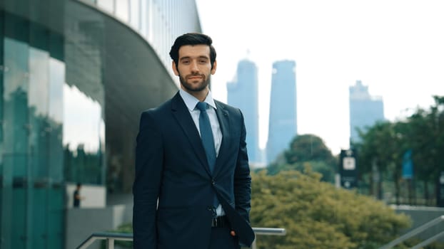 Professional businessman standing at city or park. Smiling project manager looking at camera while smiling arms with confident. Closeup of investor wearing suit at architectural building. Exultant.