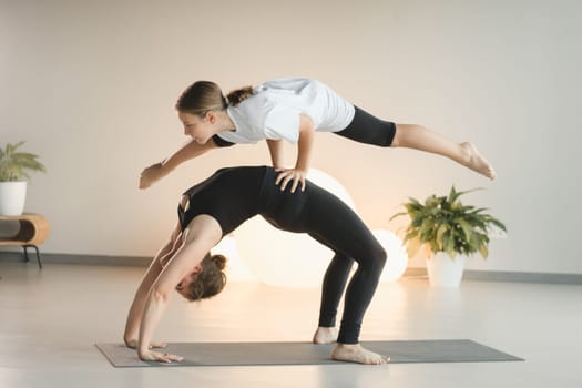 Mom and teenage daughter do gymnastics together in the fitness room. A woman and a girl train in the gym.