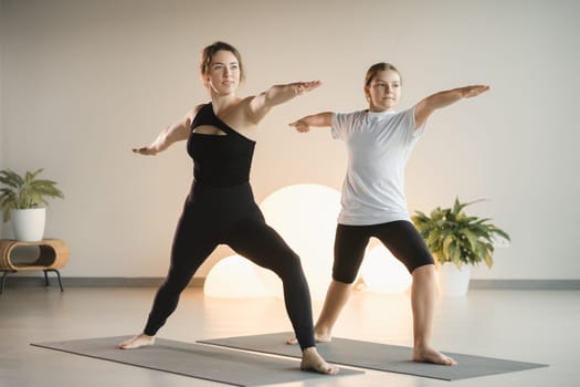 Mom and teenage daughter do gymnastics together in the fitness room. A woman and a girl train in the gym.