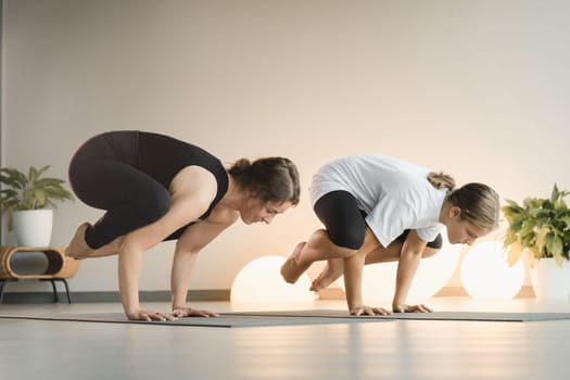 Mom and teenage daughter do gymnastics together in the fitness room. A woman and a girl train in the gym.