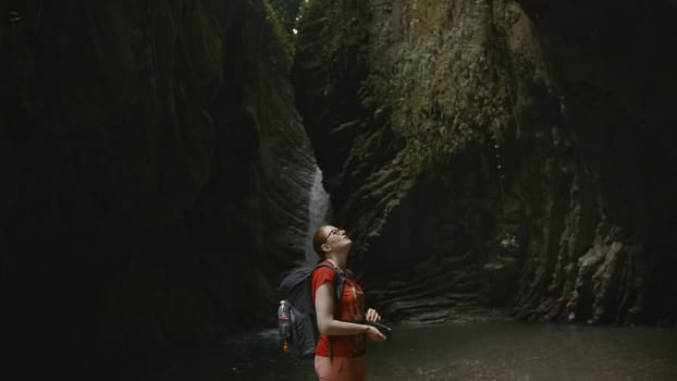 Woman at rocky cave in jungle. Creative. Hiking in rocky landscapes of wild jungle. Beautiful waterfalls and rocks in dark green forest.