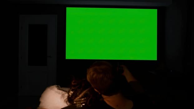 Viewing on a large projector at home. Media. A young couple embracing on the couch looking at a green screen. High quality 4k footage