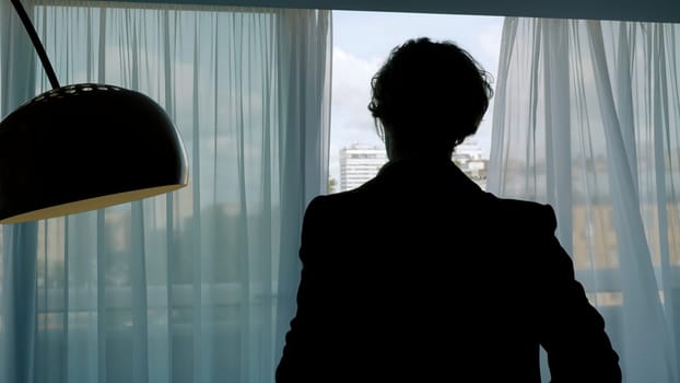 Young businessman in a the hotel room. Action. Young attractive man in black suit standing indoors and looking thoughtful