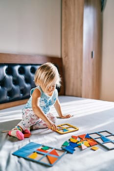 Little girl puts together a puzzle in a cardboard tablet on the bed. High quality photo