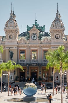 Monaco, Monte-Carlo, 21 October 2022: Square Casino Monte-Carlo at sunny day, wealth life, tourists take pictures of the landmark, pine trees, blue sky. High quality photo