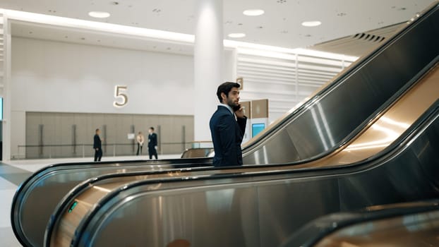 Professional leader walking to escalator while calling his business team about startup project. Smart business man talking about marketing plan while talking to colleague. Business team. Exultant.