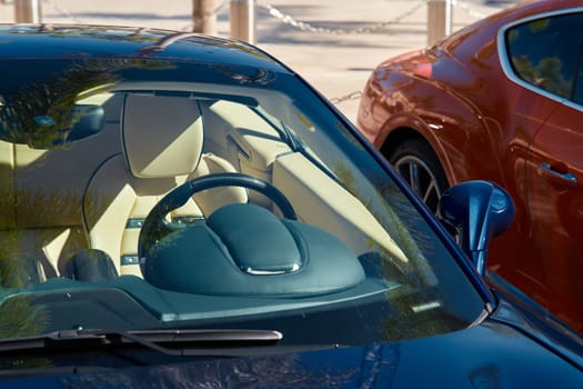 Two expensive sports cars stand side by side in sunny weather, a view of the bright interior through any glass. High quality photo