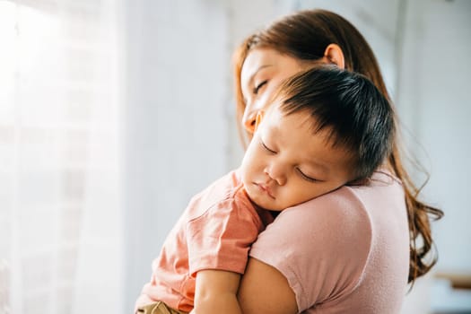 In the sanctuary of their home an affectionate Asian mom leans in to hug and cuddle her tiny sleeping infant celebrating a heartwarming family moment filled with the joy of parenthood.