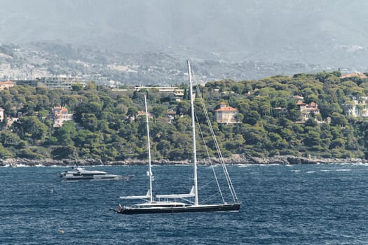 Monaco, mega yacht and huge sail boat are in sea at sunny day, island is nearby, huge motor boat, wealth life of billionaires, mountains on background. High quality photo