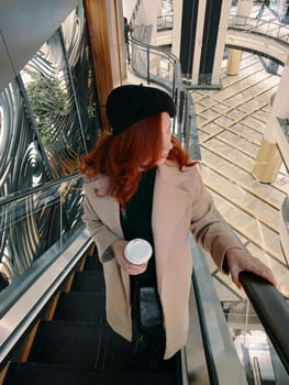 Shopping time. Red-haired woman on the escalator.