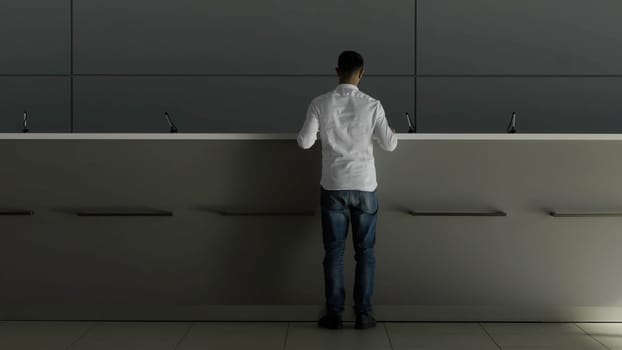 Minimalistic interior of a hotel lobby with the reception desk. HDR. Rear view of a businessman in white shirt going to the receptionist and asking something