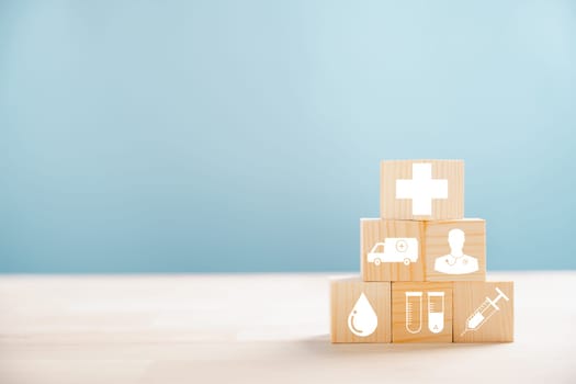 Pyramid of wooden cubes representing healthcare and insurance ideals. Crowned with a medical insurance icon on white background, offering copyspace for Health Insurance theme.