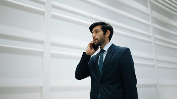 Skilled manager using phone call to contact colleague about project. Handsome male leader calling his business team to report and discuss about sales while standing at white background. Exultant.