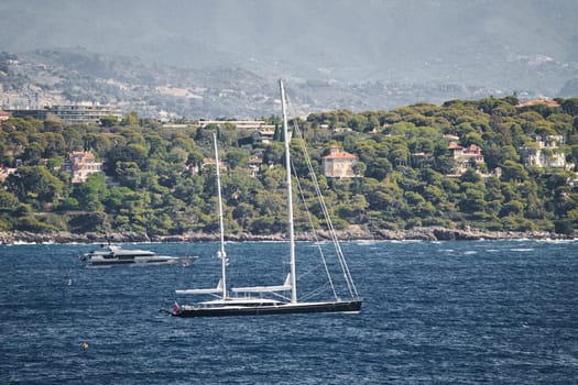 Monaco, mega yacht and huge sail boat are in sea at sunny day, island is nearby, huge motor boat, wealth life of billionaires, mountains on background. High quality photo