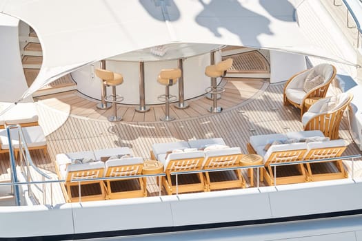 Close up footage of a relaxation area on the open teak deck of an expensive megayacht at sunny day, with awnings stretched over the deck to protect from the sun, wealth life, table and chairs. High quality photo