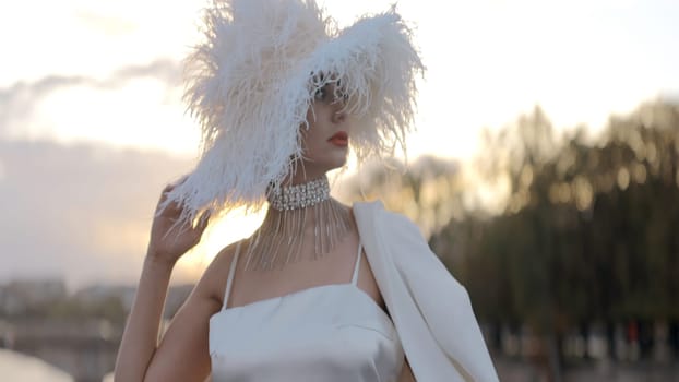 Elegant woman with stylish hat. Action. Gorgeous woman in white with designer hat. Elegant woman in unusual hat posing on background of summer city.