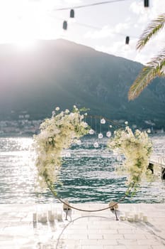 Round wedding arch with hanging spherical candlesticks stands on the pier. High quality photo