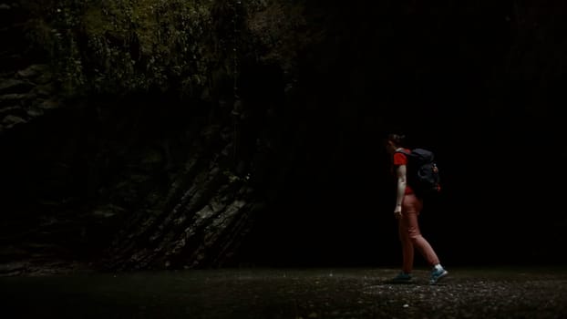 Woman walking near small lake on a rainy day inside the gorge. Creative. Hiker with a backpack against the mountain covered by moss