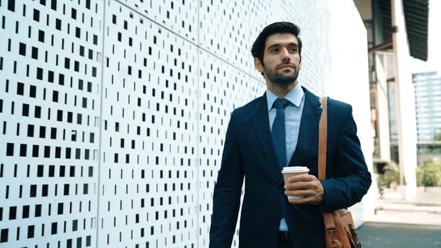 Skilled business man walking in suit outfit while holding coffee cup. Professional manager standing near architectural building. Going to working in morning, seeking for successful job. Exultant.