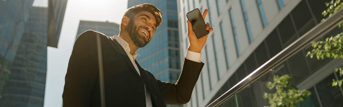 Stylish businessman is standing with laptop on office terrace and looks away. High quality photo