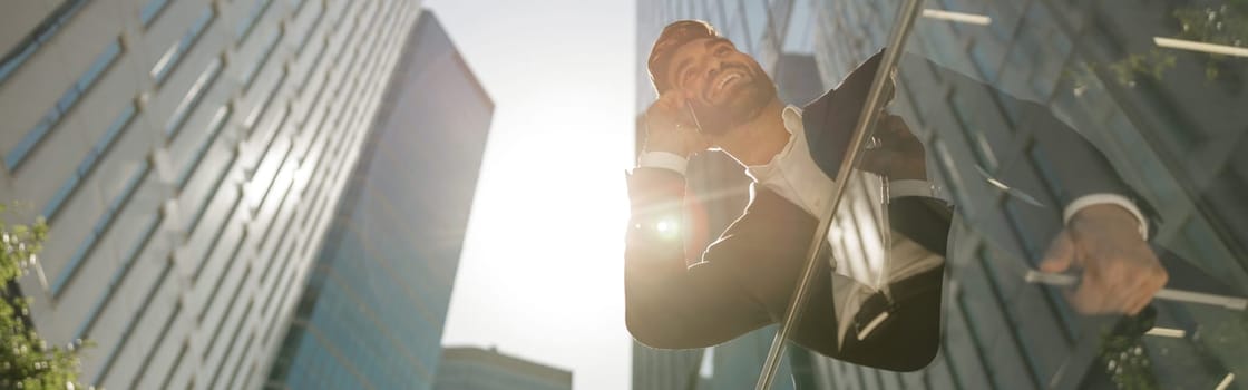 Stylish businessman is standing with laptop on office terrace and looks away. High quality photo