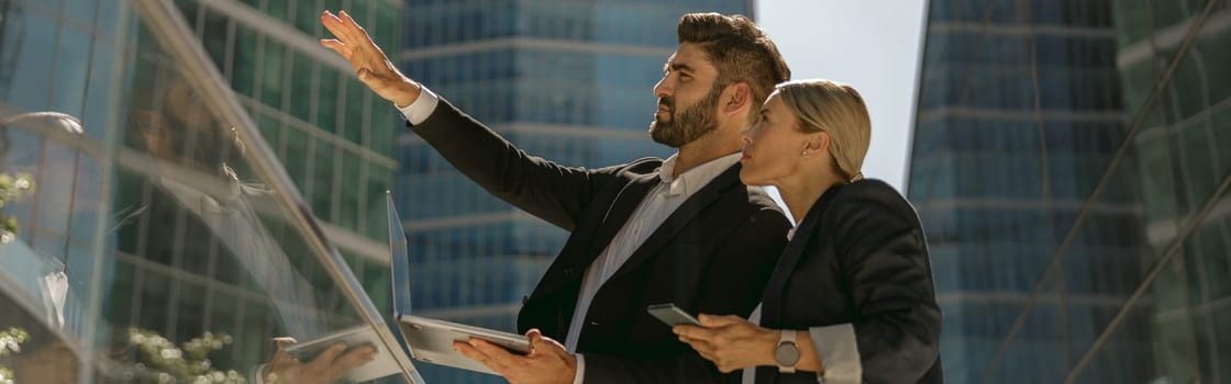 Businessman showing something to his female colleague while standing on office terrace
