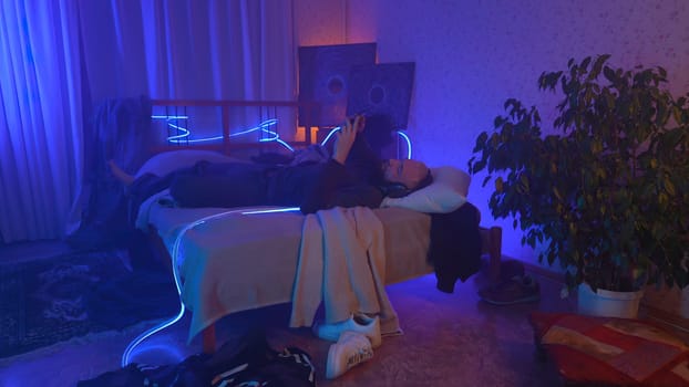 Stressed man lie on the bed at home while holding his head neon background. High quality photo