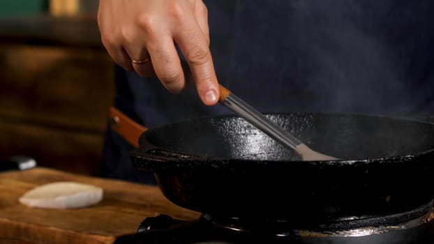 Close up of male cook frying sauce and adding sugar or salt in a black iron pan. Process of food preparation at the restaurant.