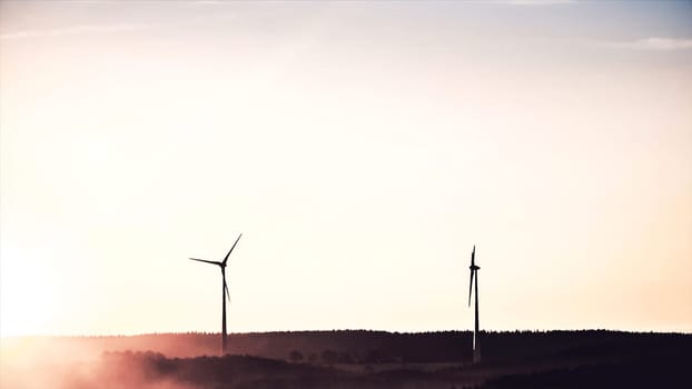 Abstract power windmills on the horizon and a beautiful, golden sunset landscape. Clean and ecological energy generated with the wind of nature through wind turbines, ecology concept