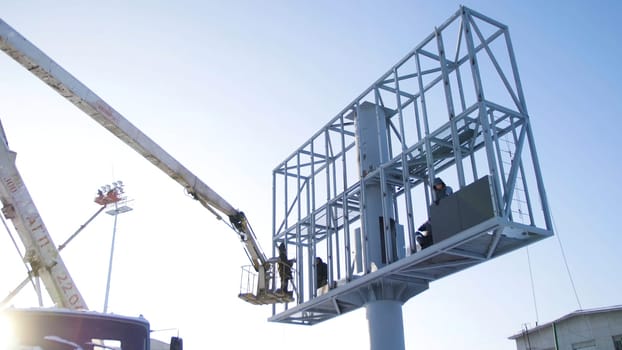 Builder on a Lift Platform at a construction site. Men at work. construction worker assembling scaffold on building site. Men assemble Billboard on tap.