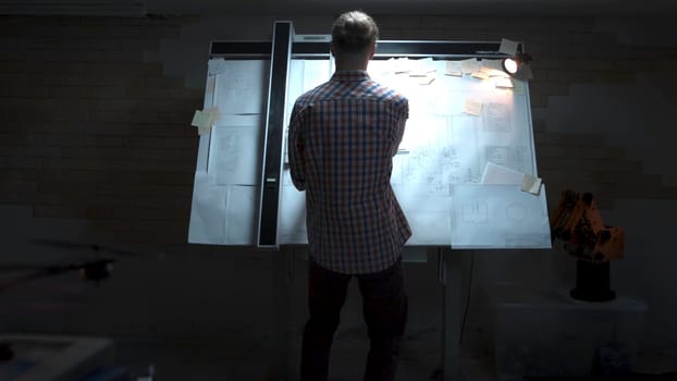 Young engineer standing at the white board with drawing and plan back view. Male architect standing at drawing board and floor plan with pencil in hand at office.