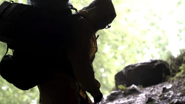 Young explorer standing in a cave with climbing equipment ready for action, travelling and extreme concept. View from the inside of the cave with climbing person.