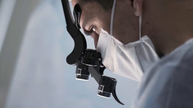 Surgeon head with professional glasses at work. Close up side view of a doctor in glasses with binocular magnifiers examines something at laboratory.