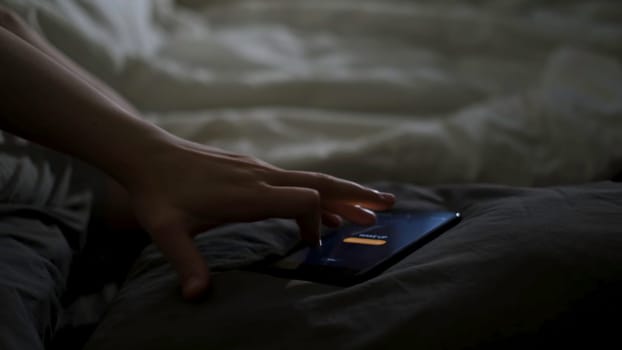 Close up of sleeping man being woken up by his phone lying on the bed. Male hand trying to turn off the alarm clock lying near on a blanket at home early in the morning.