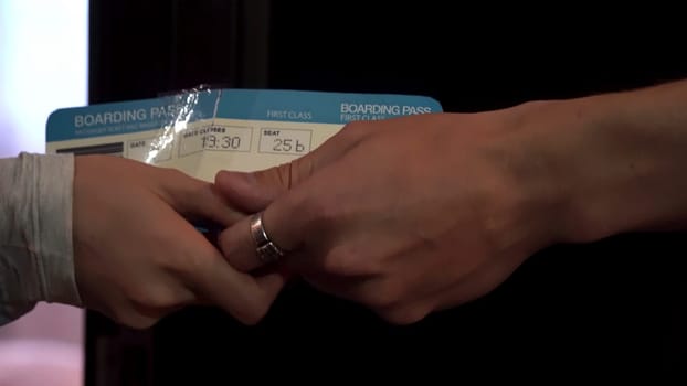 Close up for loving couple hands giving air tickets and stroking fingers. Man hands passing plane tickets to a woman hands with tenderness, side view