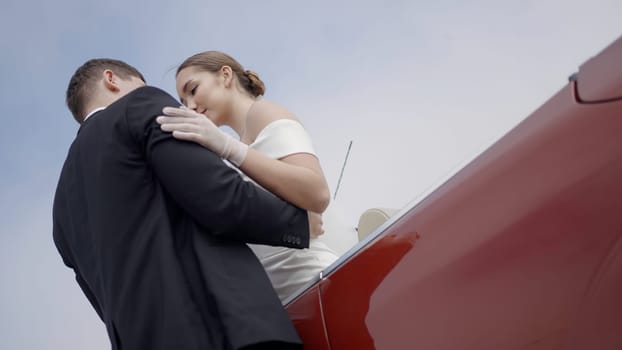 A young beautiful couple posing for a shoot . Action . A pretty girl with a white hairstyle and a man in a suit kissing newlyweds standing next to a red car. High quality 4k footage