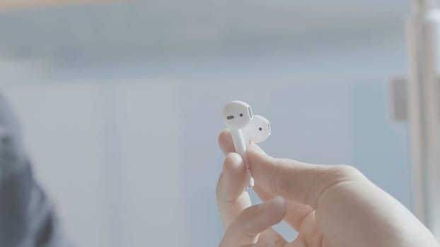 Close-up of wireless headphones in hands. Stock. Man passes pair of white wireless headphones. Stylish modern Bluetooth headphones.