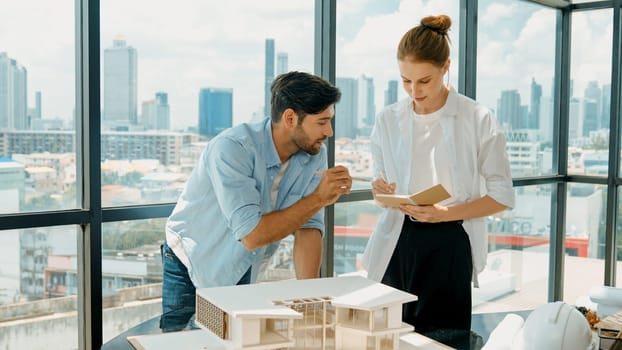 Skilled architect engineer team discussion about house model construction. Smart interior designer sharing, talking about building design while beautiful coworker taking a note. Design. Tracery